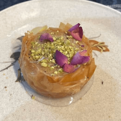 syrup-soaked round golden puff pastry close-up with crushed nuts & petals on top
